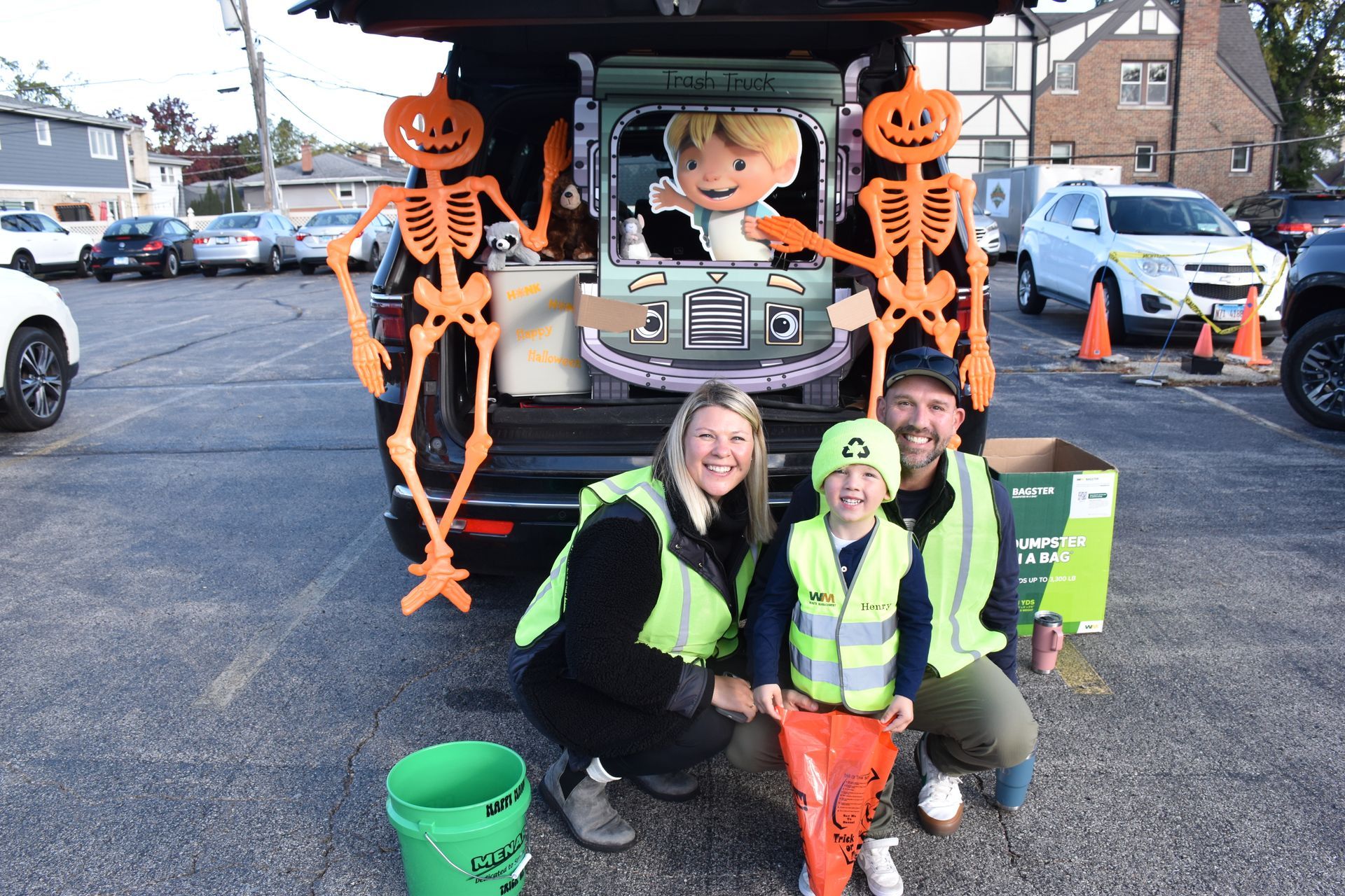 Halloween display with two orange skeletons, a pumpkin figure, and three people posing in front of it