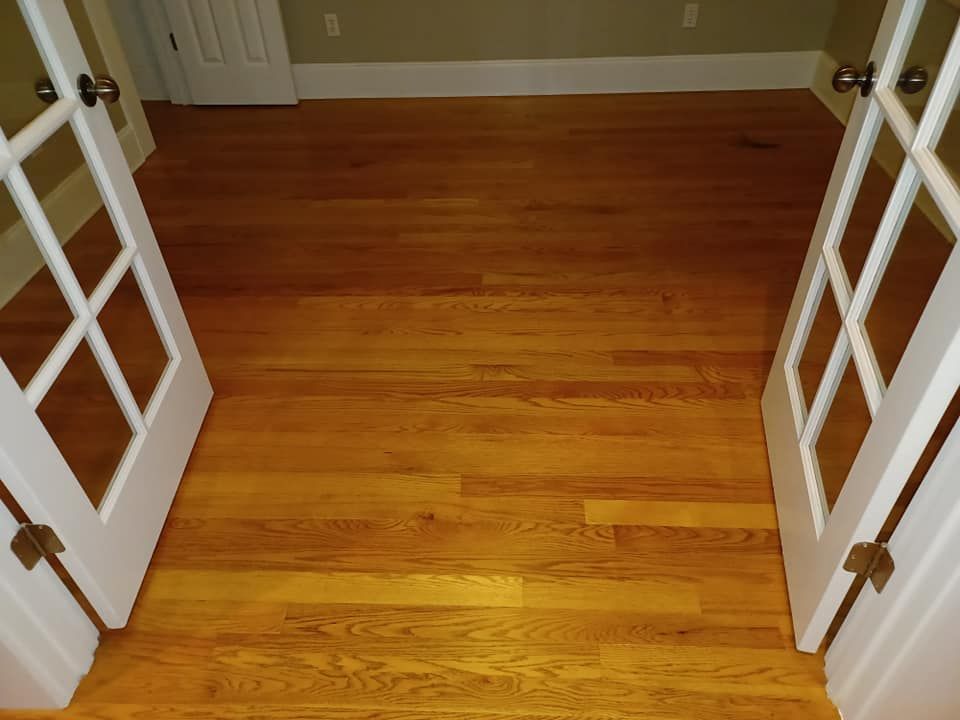 Hardwood flooring in a room viewed through an open set of white French doors, with light green walls and white baseboards.