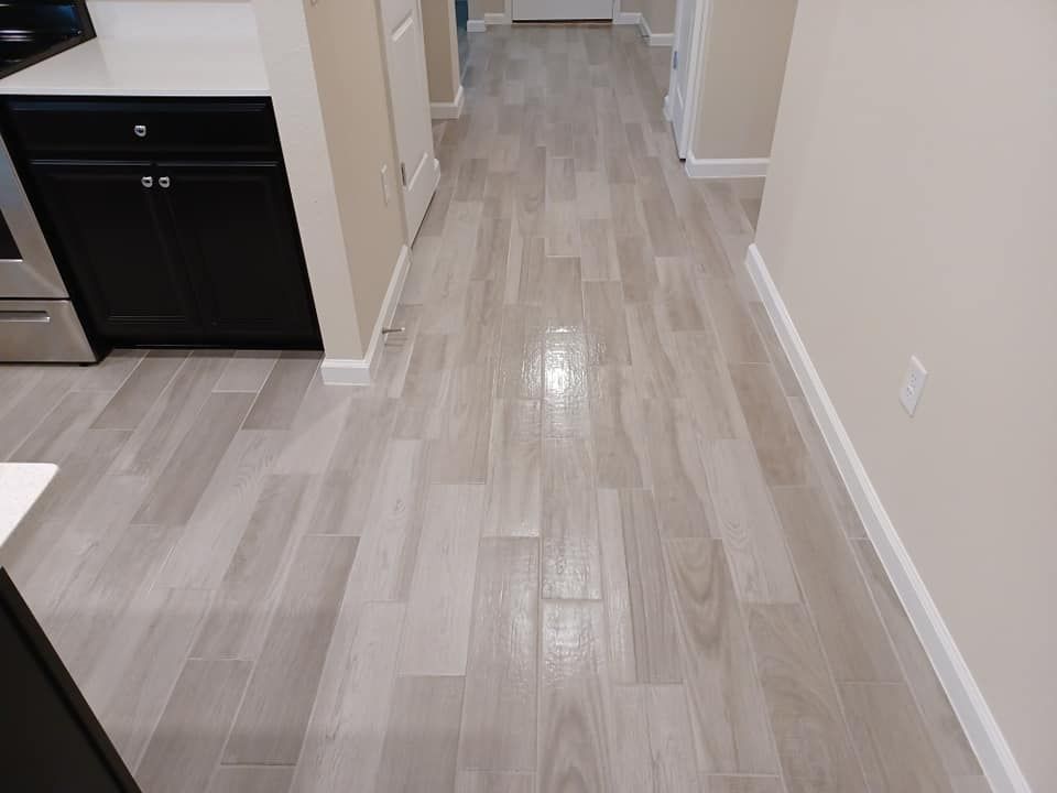 Light gray wood-look floor planks installed in a hallway next to black kitchen cabinets.