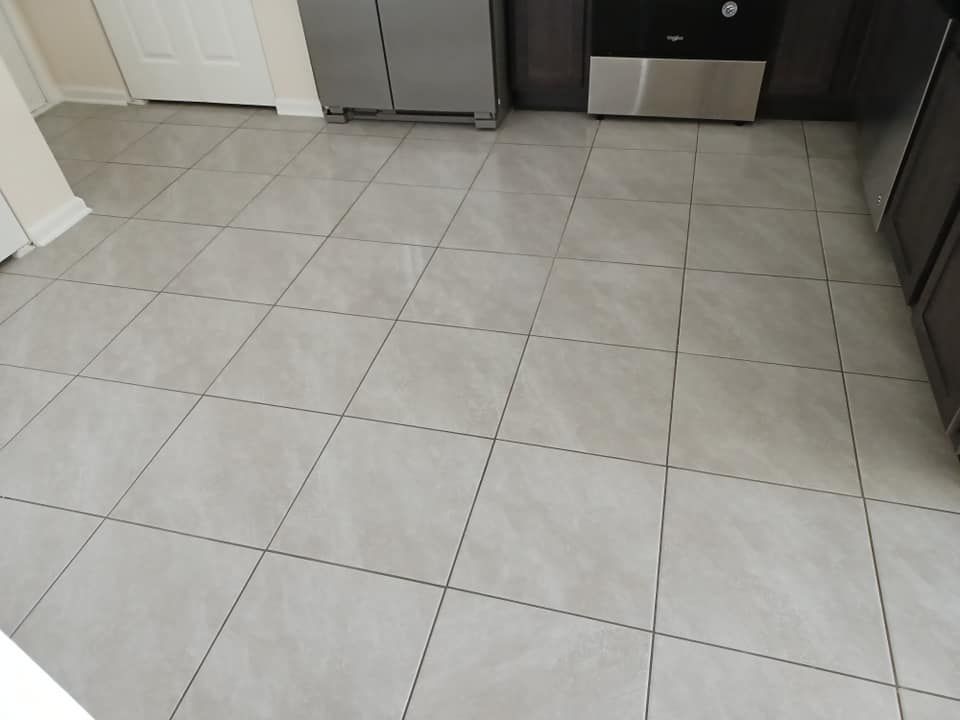 A high-angle view of a kitchen floor with large, square, light-gray marble-patterned tiles and dark grout lines.