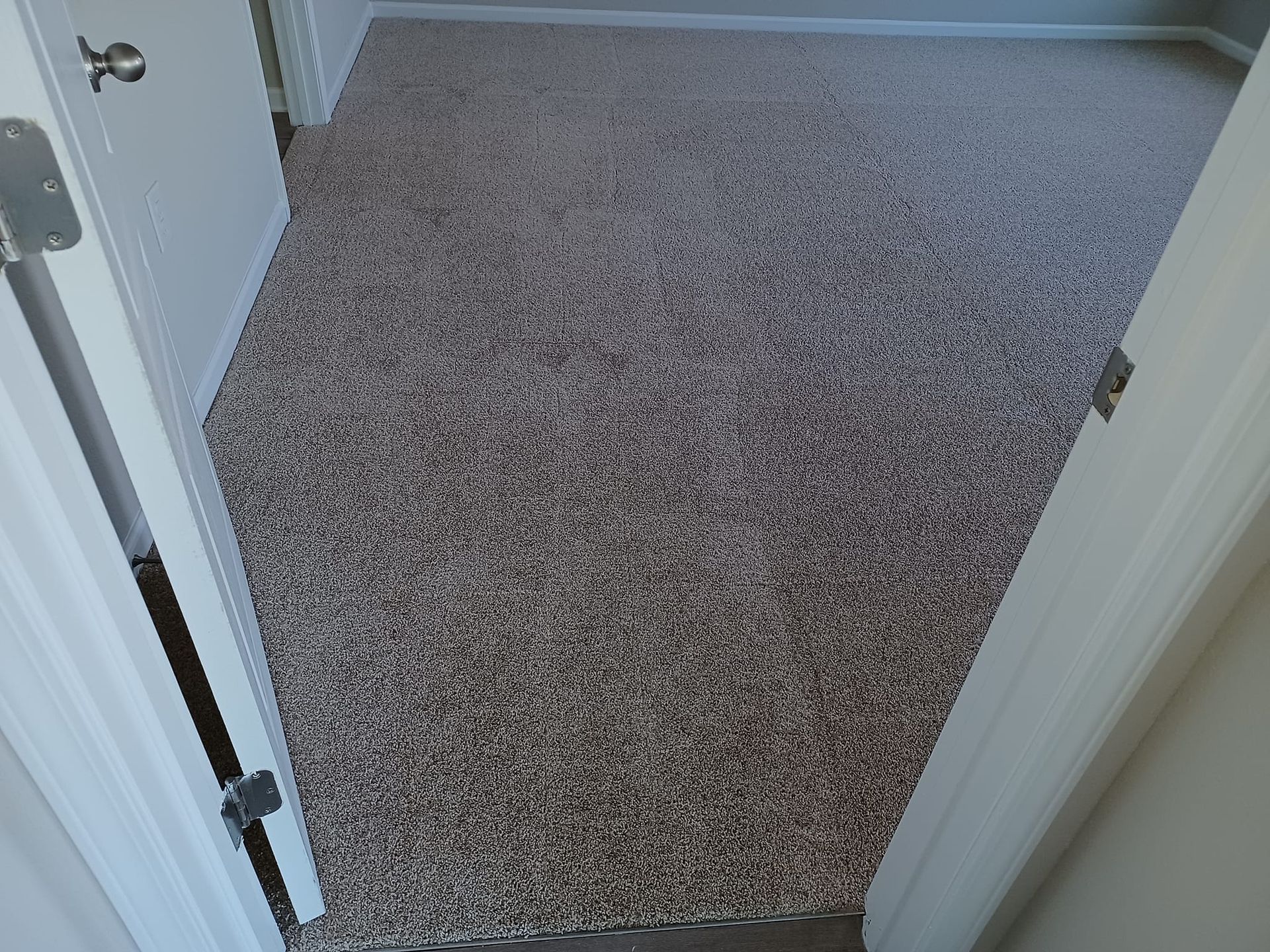 A view from a doorway looking into an empty room featuring wall-to-wall, multi-colored speckled carpeting.