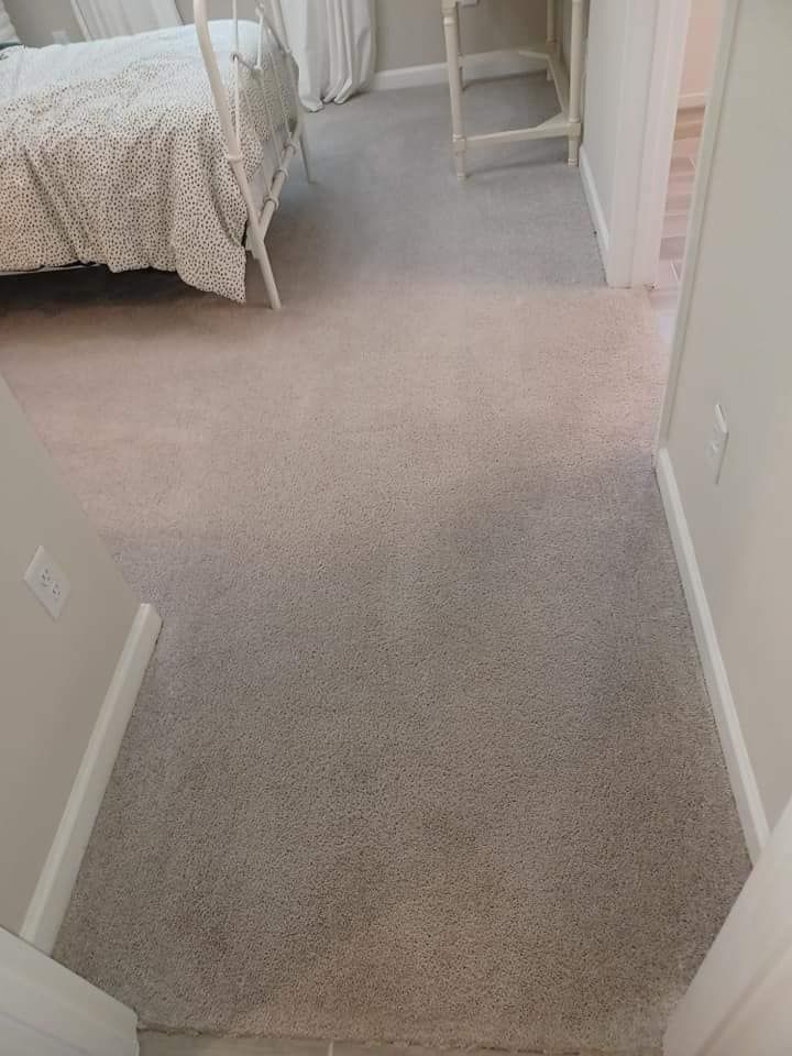 A hallway floor carpeted in a mix of light and dark grey patches, leading into a bedroom with a white bed frame.