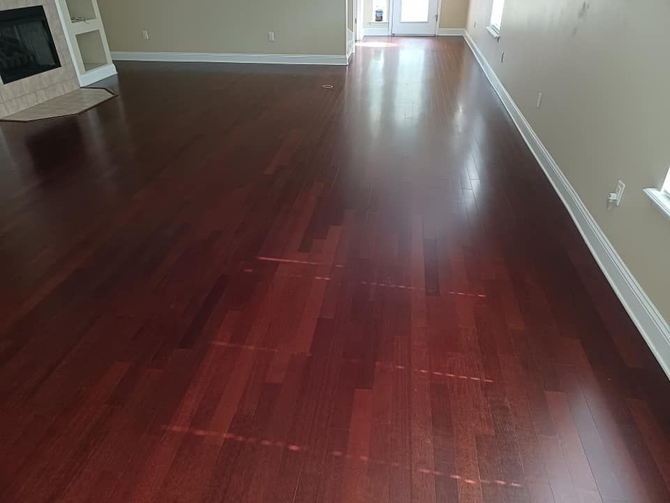 A view of a polished, reddish-brown hardwood floor in a brightly lit room with a fireplace to the left.