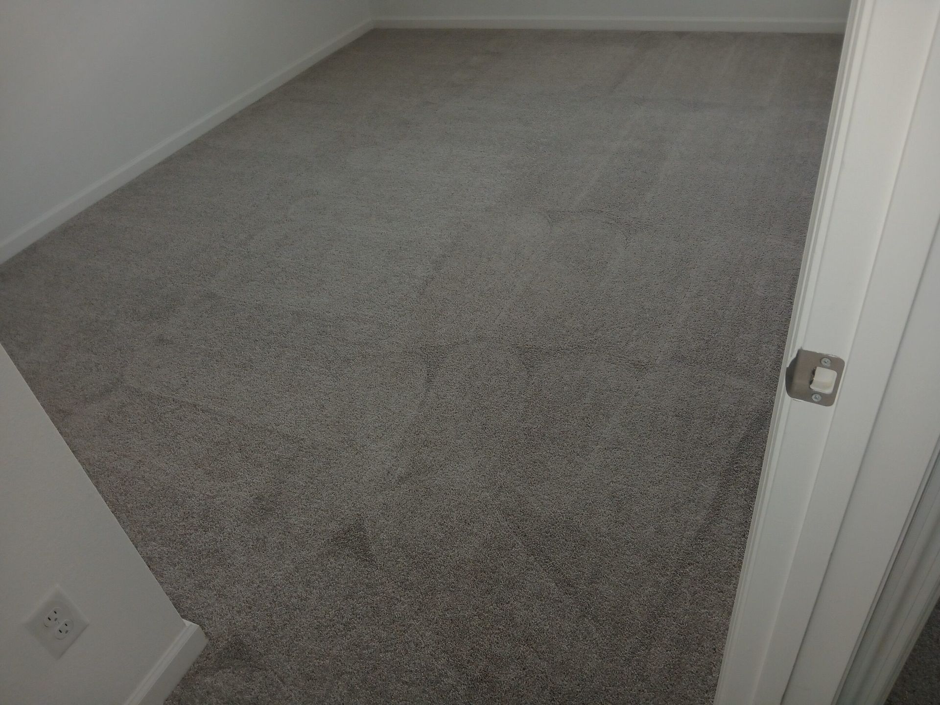 An empty room with gray carpet and white walls, viewed through an open doorway.