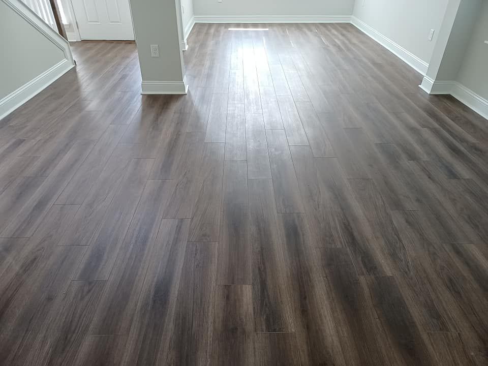A room with dark brown wood-look flooring, light grey walls, and white baseboards.