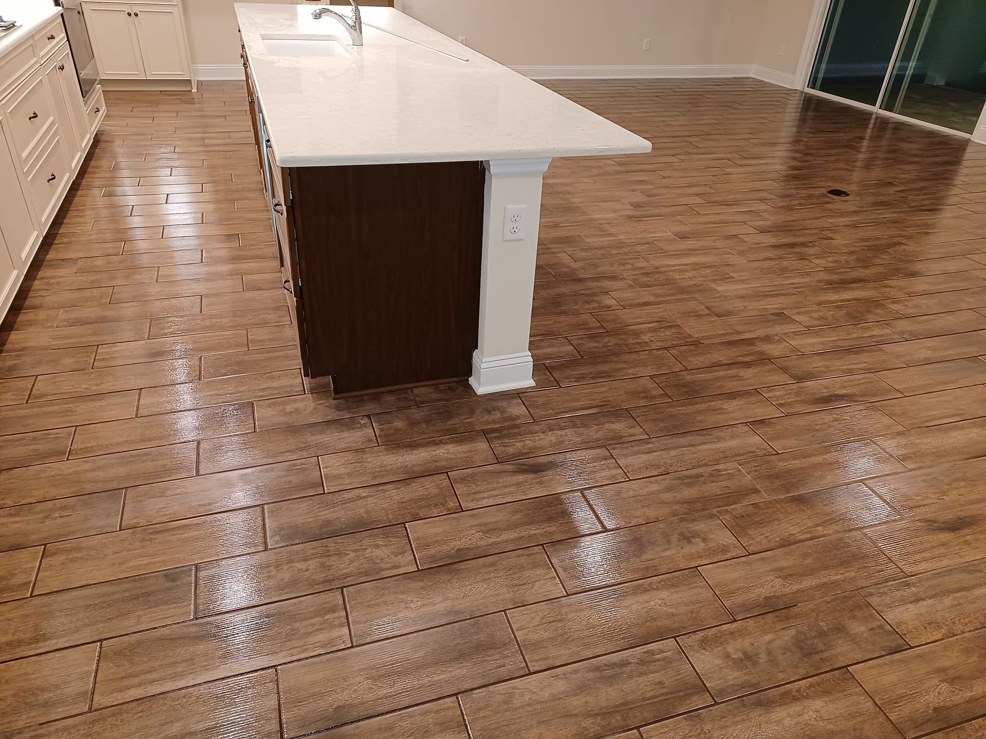 A modern kitchen island with a white countertop and dark base, situated on a glossy wood-look tile floor.