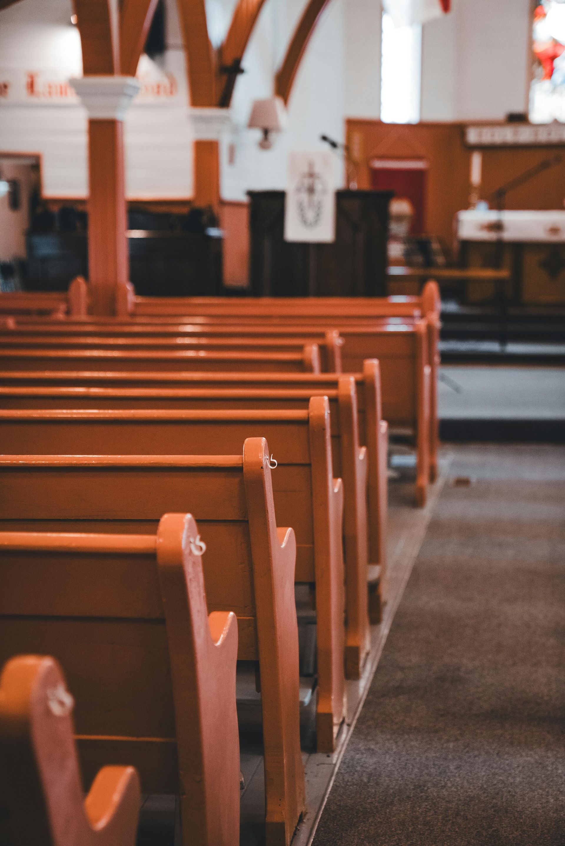 A view down the central aisle of a church, showing rows of empty wooden pews leading toward the altar area.