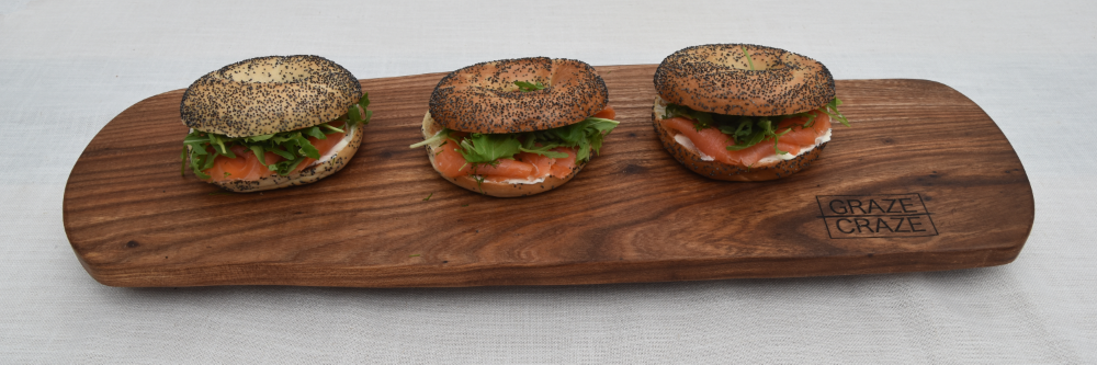 Three bagels with smoked salmon sitting on a wooden grazing board.