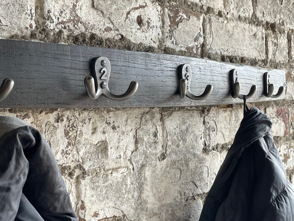 Two coats are hanging on a handmade oak barrel coat rack hung on a rustic brick wall.
