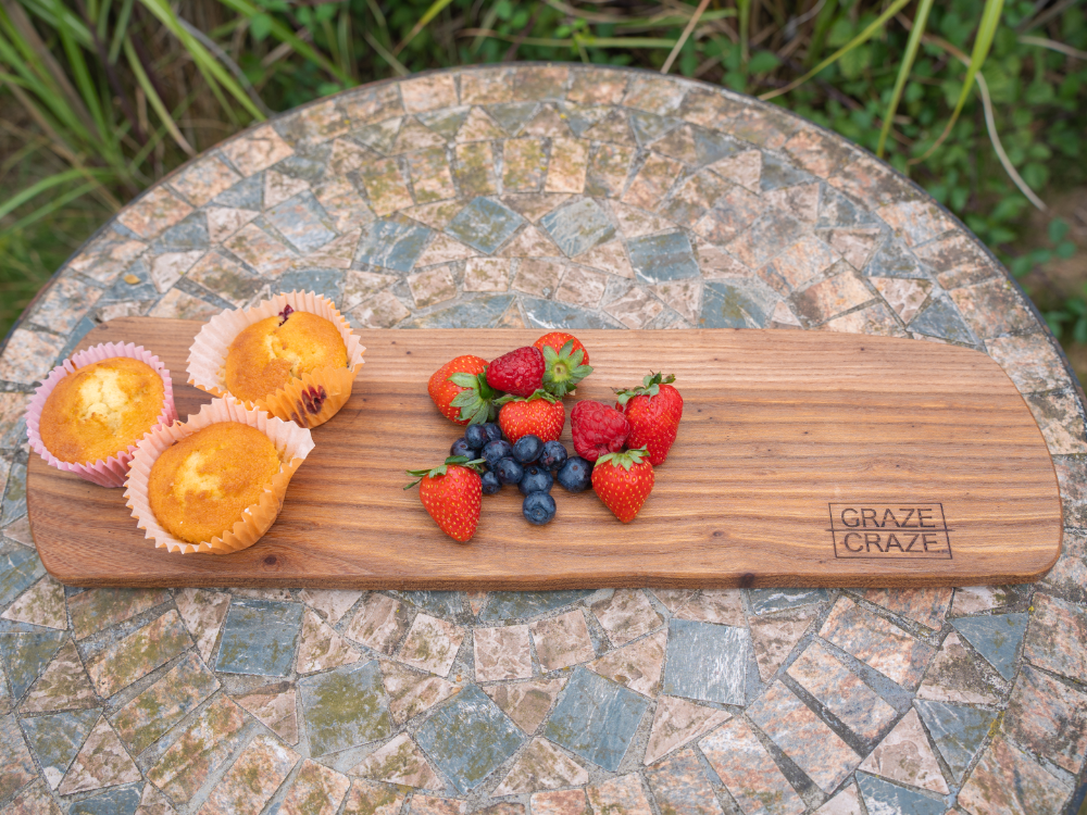 A wooden grazing board with strawberries , blueberries and muffins on it.