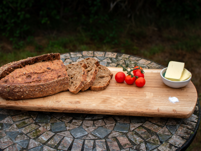 A wooden grazing board filled with a loaf of bread, tomatoes and butter.