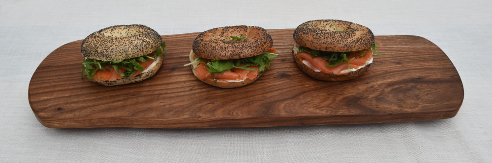Three salmon and cream cheese bagels on a wooden serving board.
