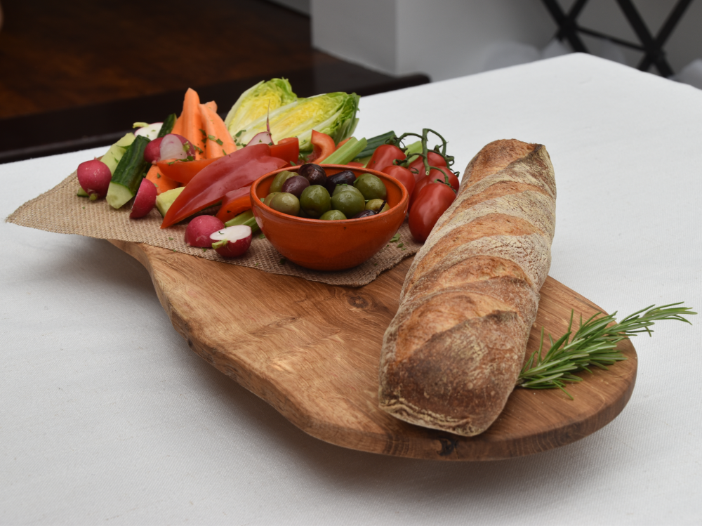 A wooden grazing board with vegetables and bread on it