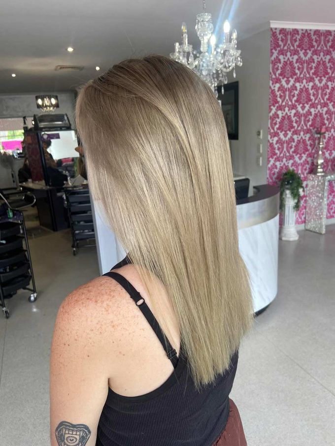 A Woman With Long Blonde Hair and a Tattoo on Her Arm is Standing in a Salon — Cosmo Hair & Beauty In Nambour, QLD