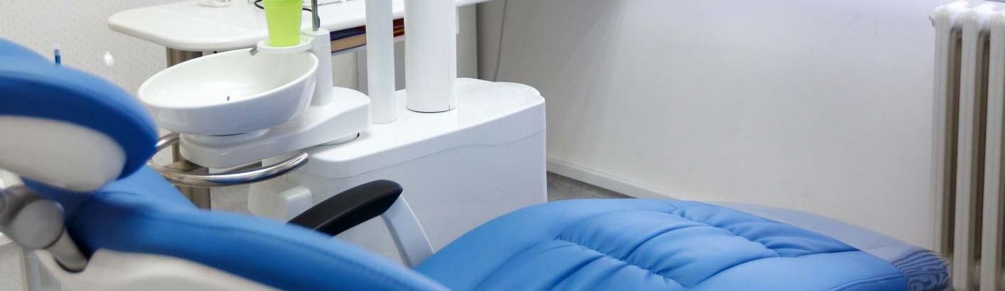 A blue dental chair is sitting in a dental office.