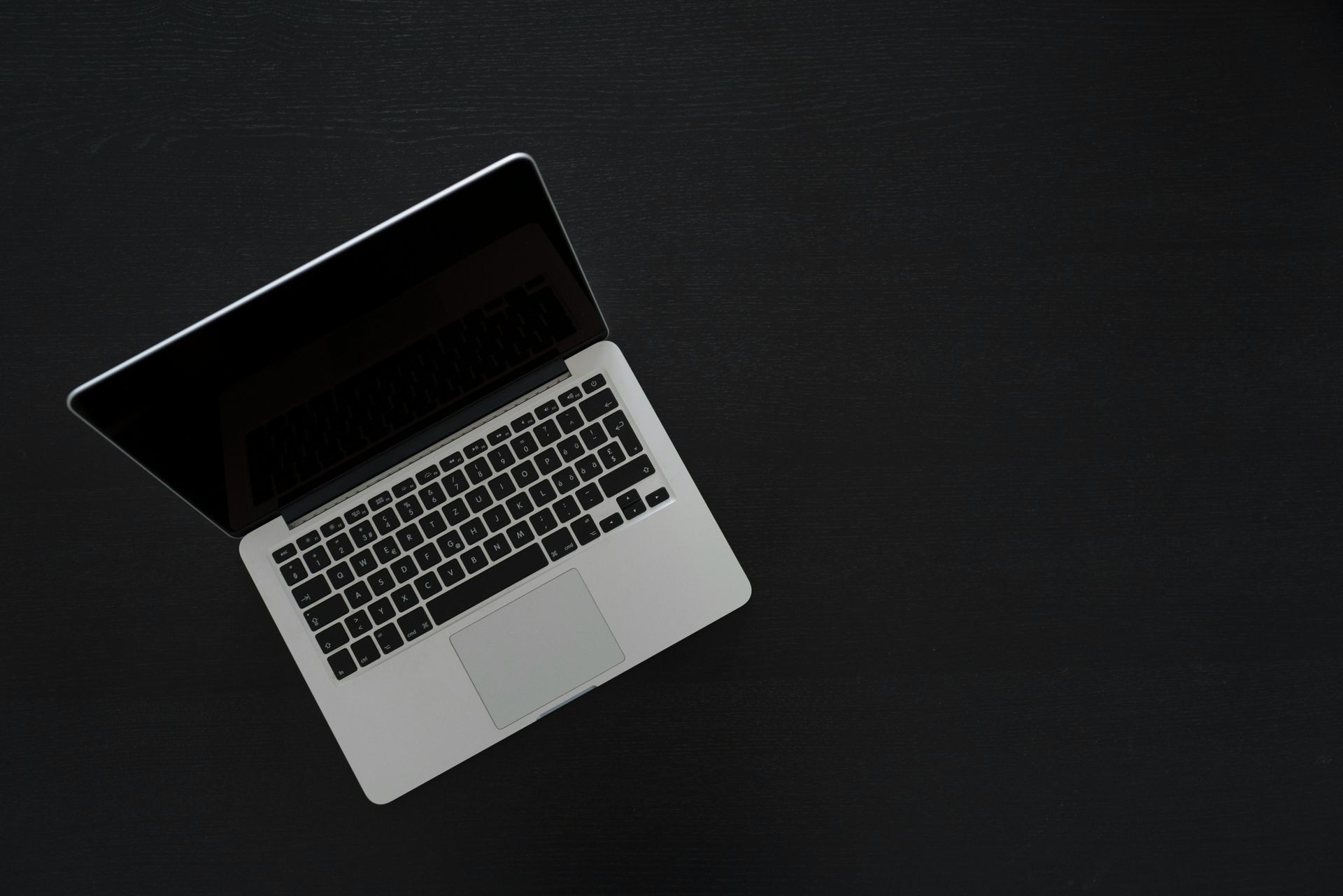 Laptop with a black screen sits open on a dark surface, top-down view.