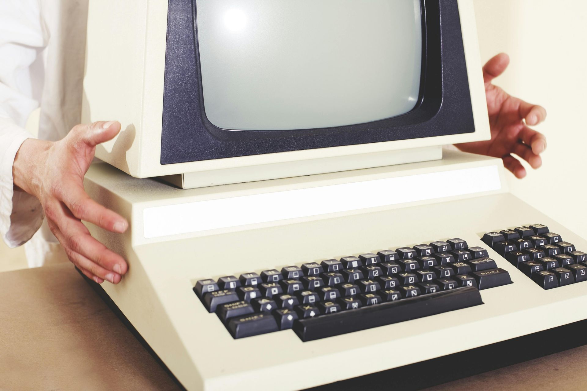 Hands holding a vintage computer, beige with a black screen and keyboard.
