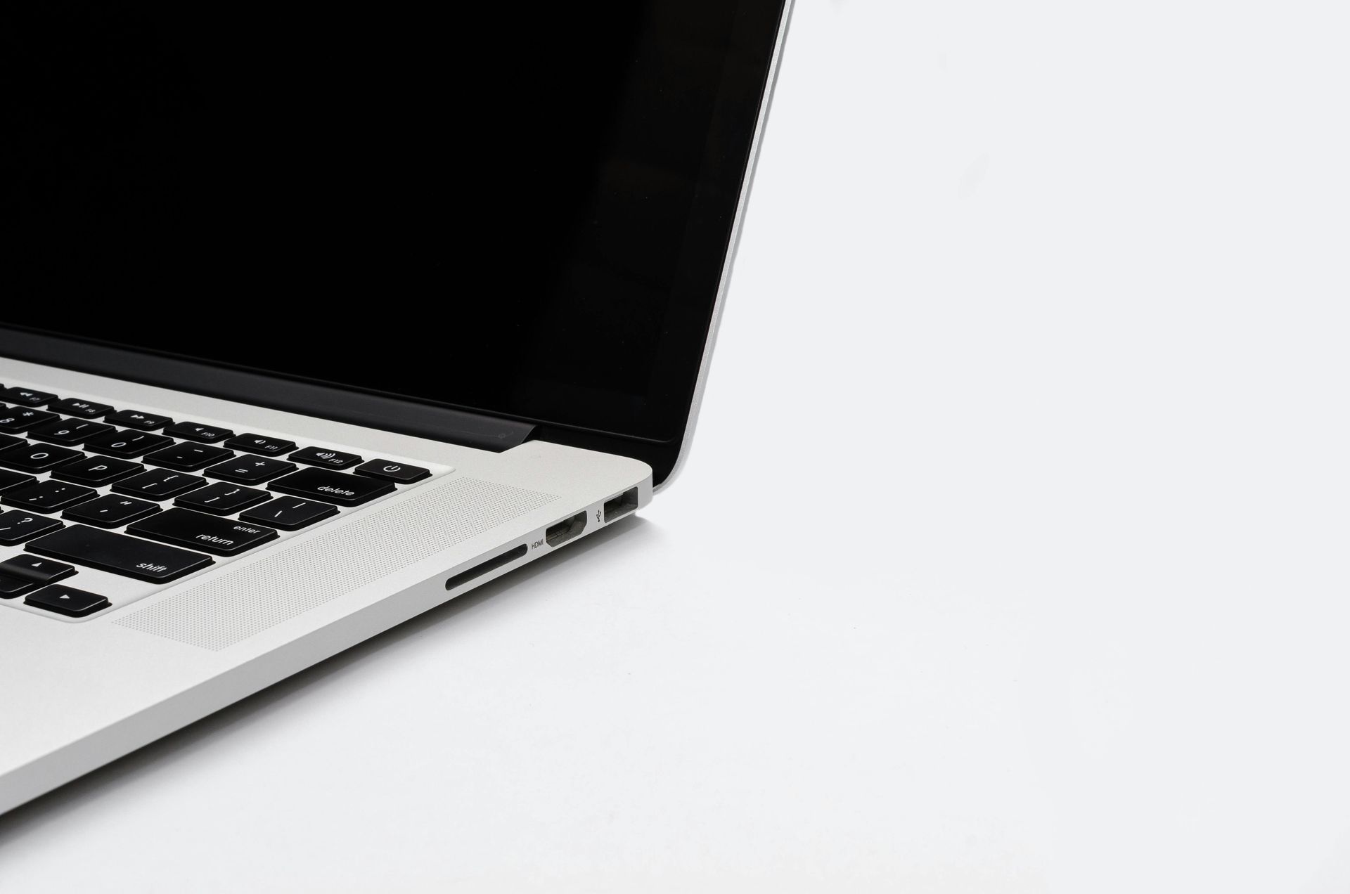 Silver laptop on a white surface, screen off, keyboard visible, angled view.