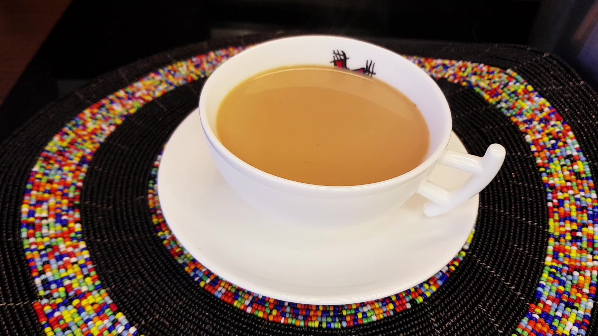 Cup of tea in a white teacup and saucer, resting on a beaded coaster.