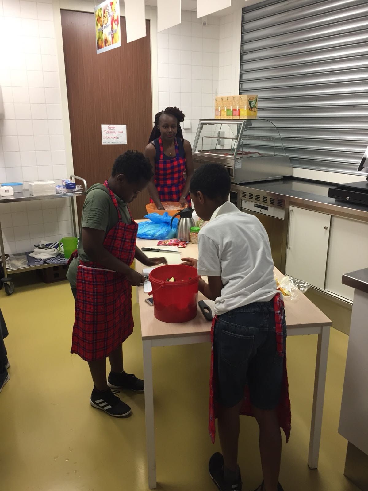 Three people wearing aprons preparing food in a kitchen.