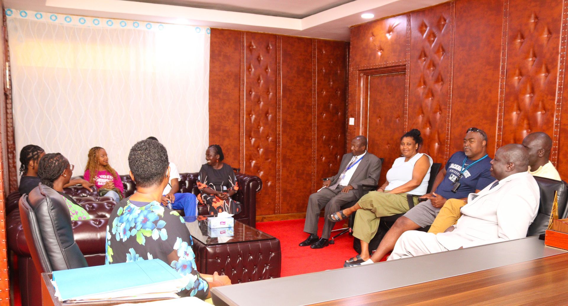 Group of people in a wood-paneled room seated for a meeting. Some are looking at each other, some are facing forward.