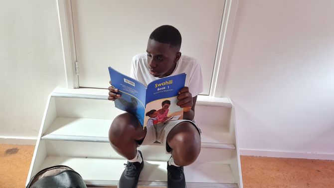 Person reading a book while sitting on stairs. White t-shirt and shorts. Blue book cover.