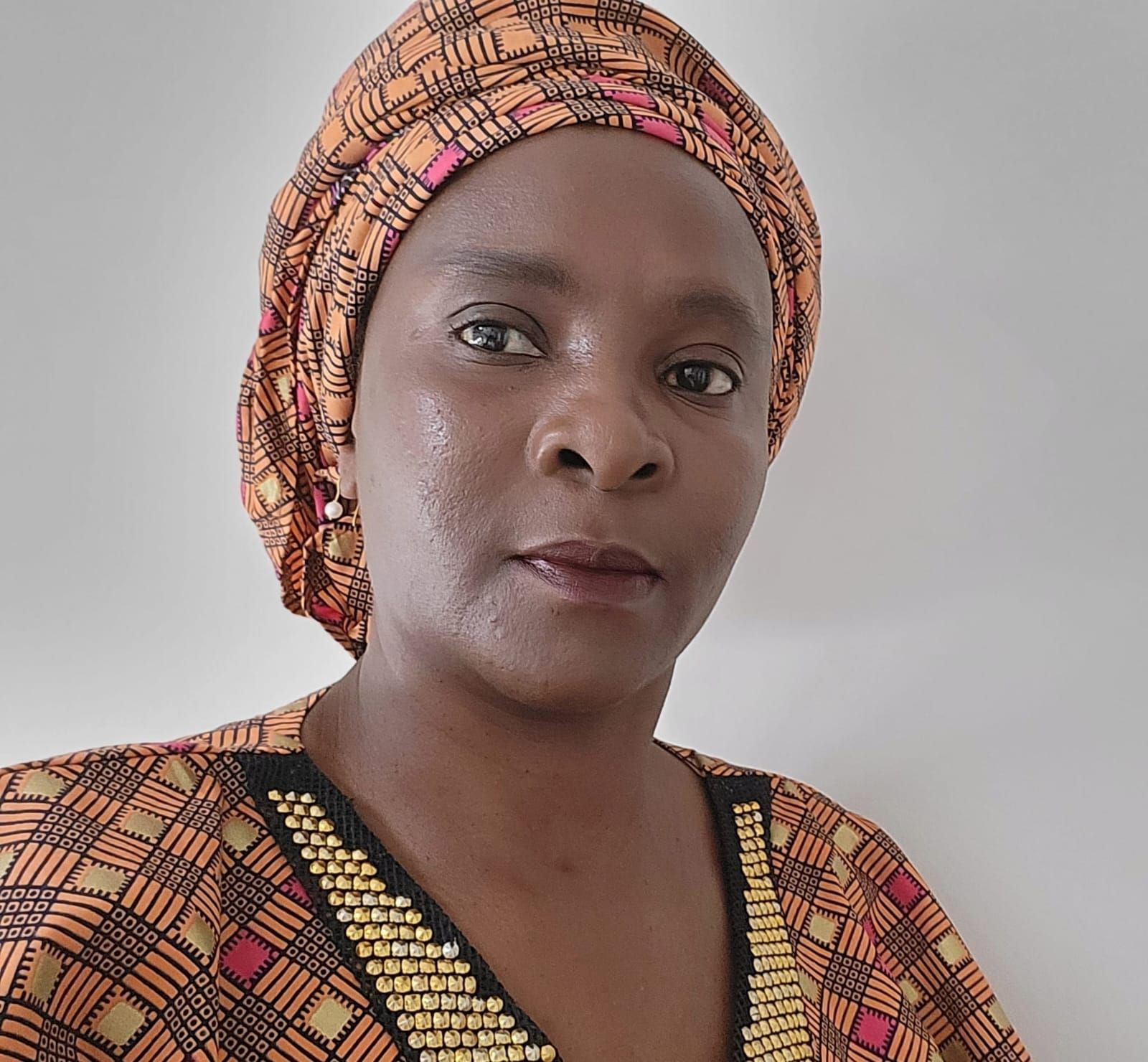 Woman wearing an orange patterned headwrap and top, looking directly at the viewer.