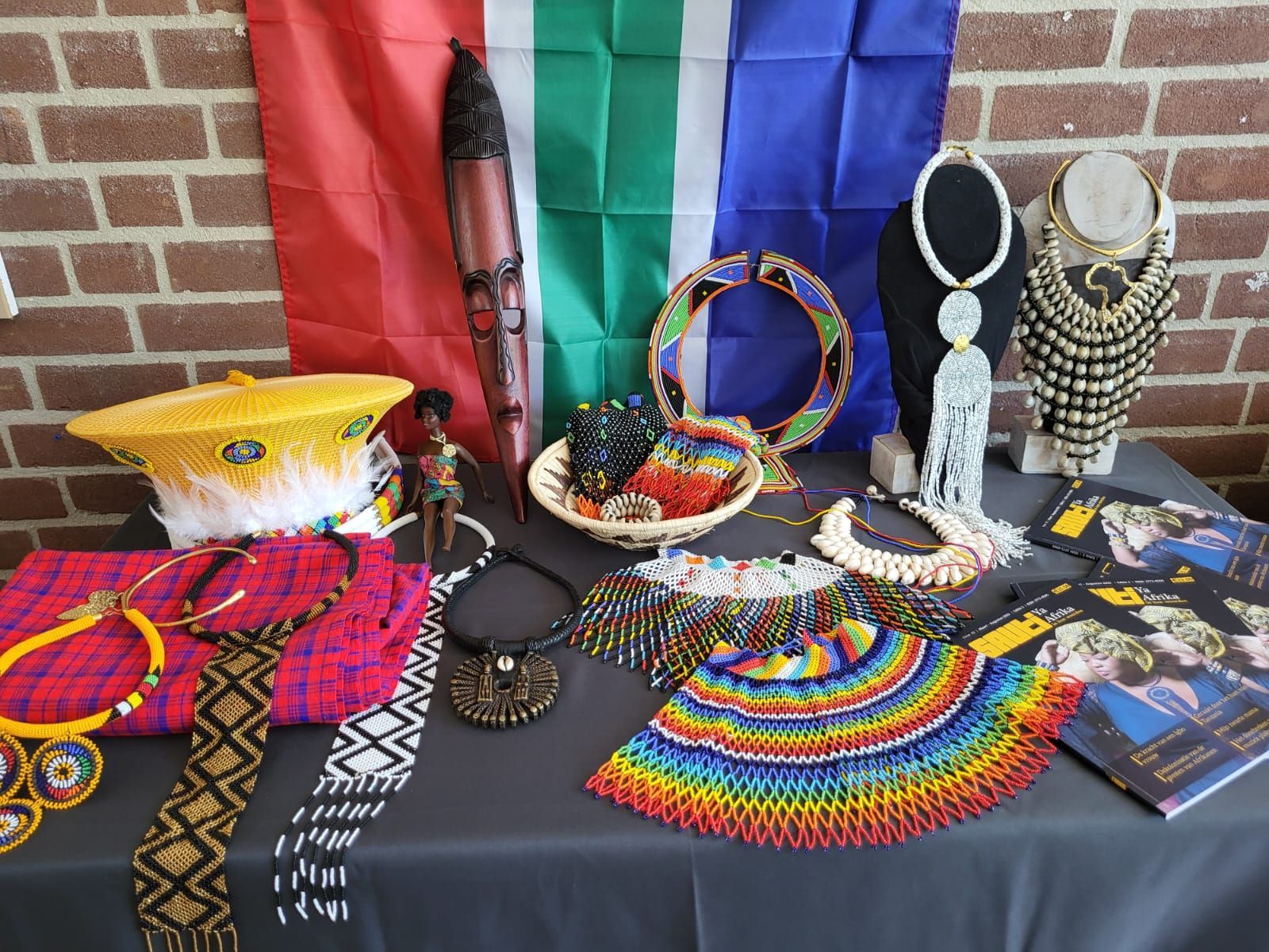 Tabletop display with South African flag background, featuring colorful beaded jewelry and artifacts.