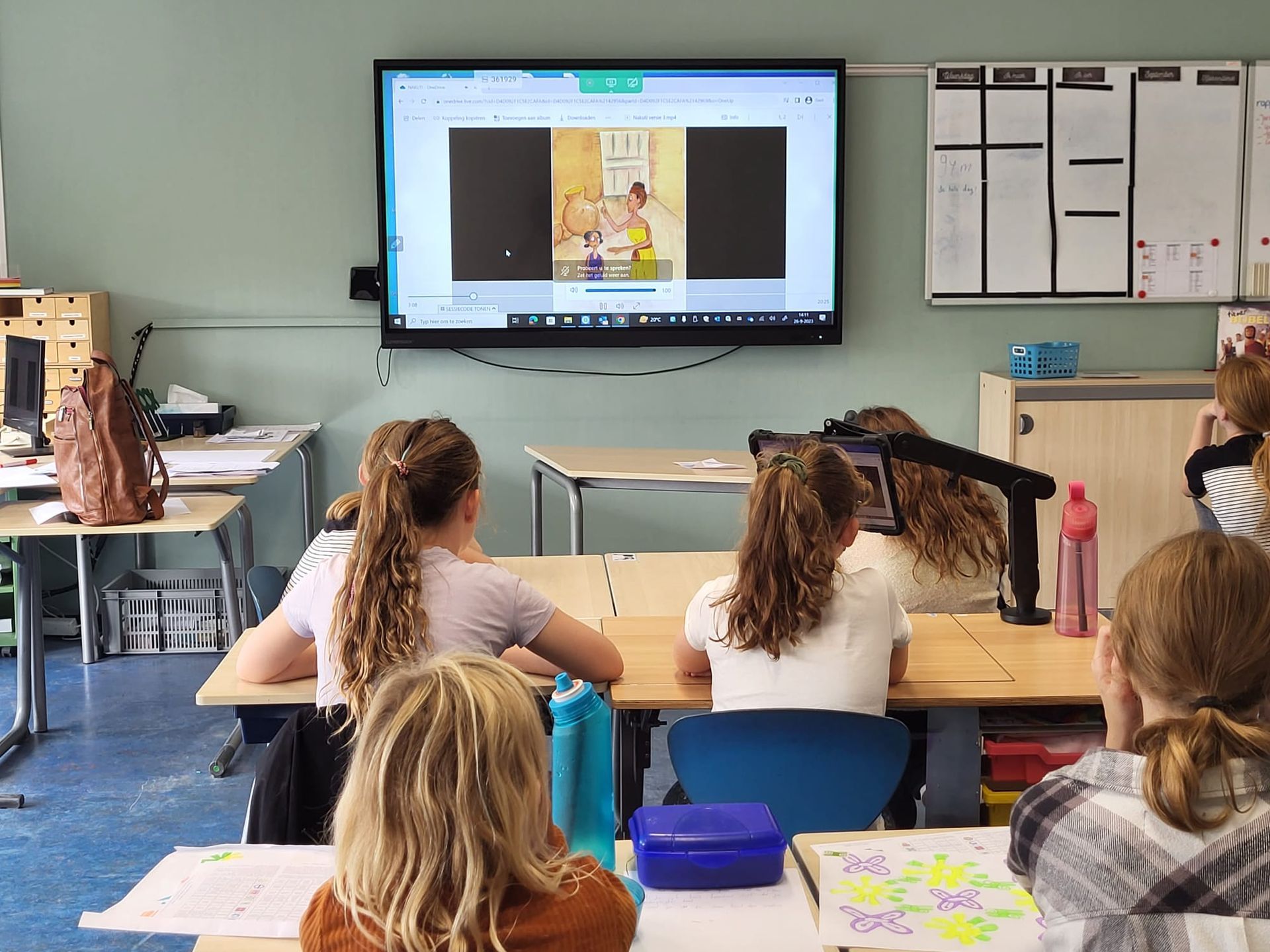 Children in a classroom looking at a screen displaying a book illustration.