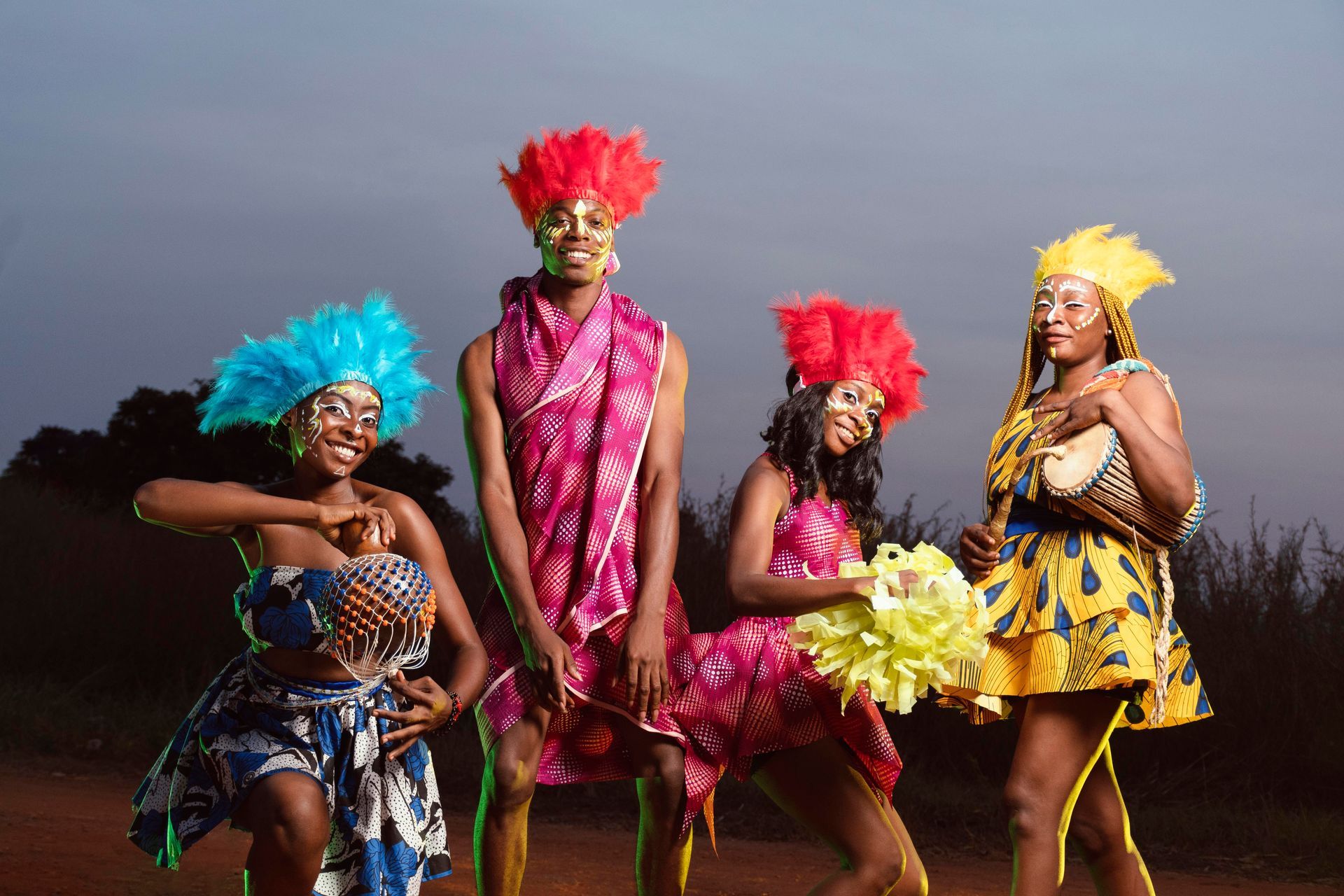 Four people in colorful African attire with headdresses, posing outdoors.
