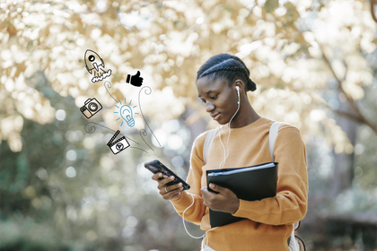 A woman is holding a book and looking at her cell phone.