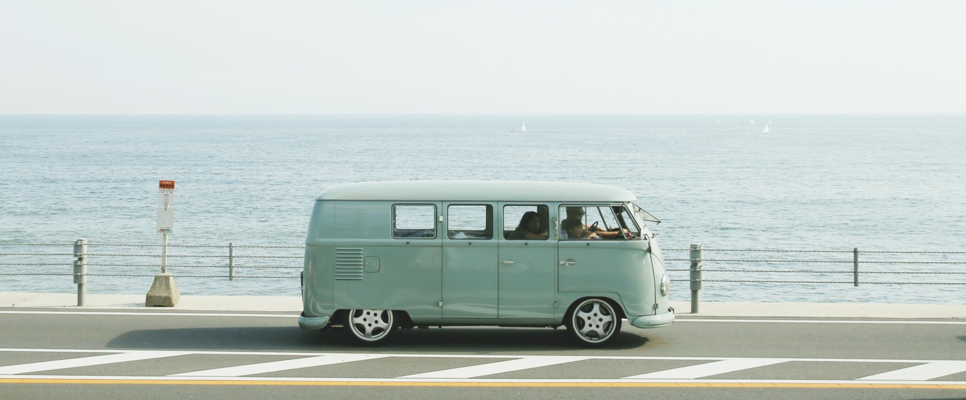 A van is driving down a road next to the ocean.