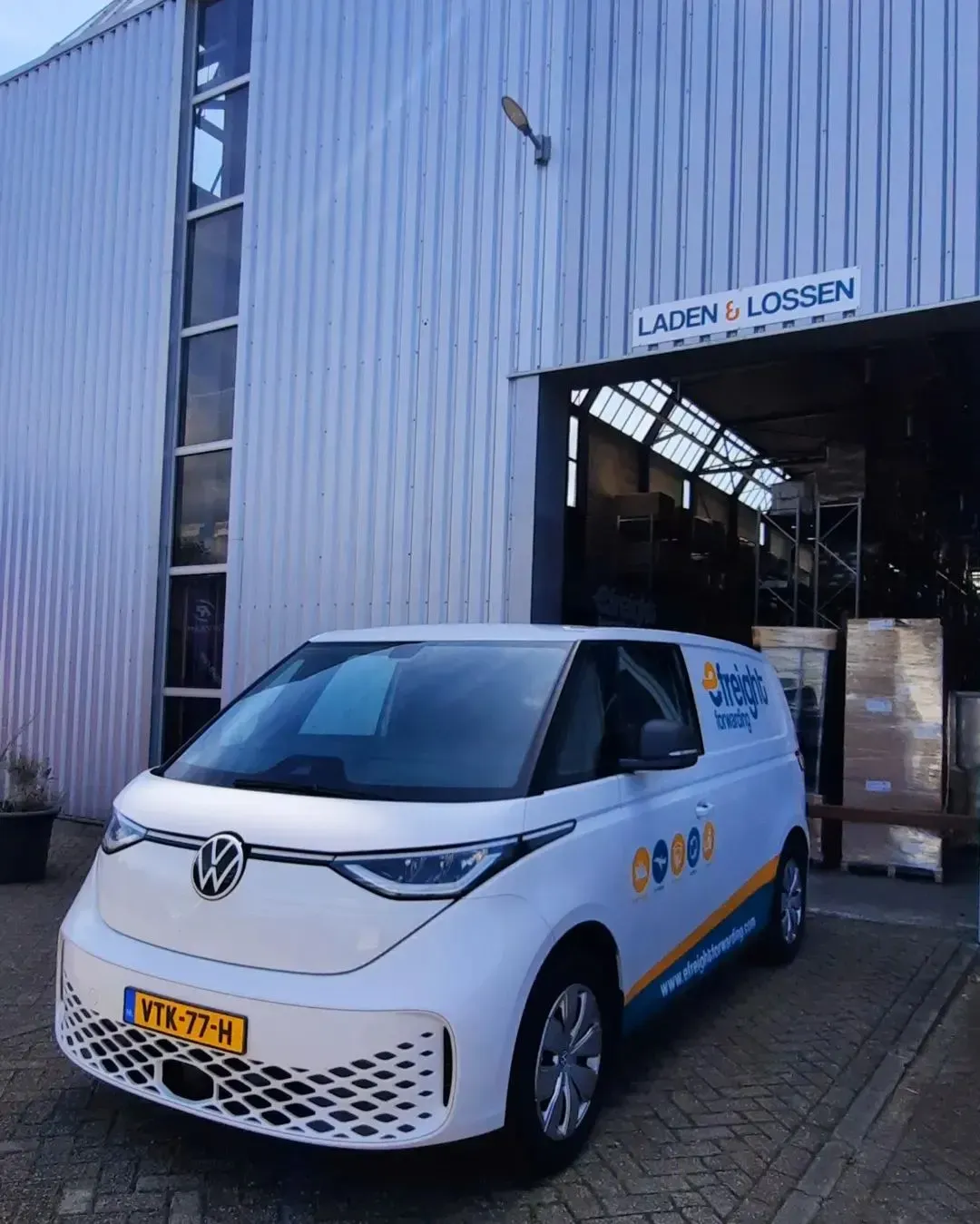 Voor een gebouw staat een wit busje geparkeerd.