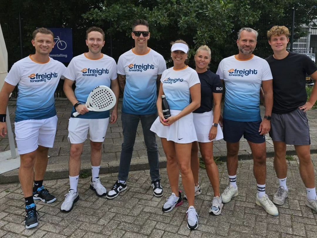 een groep mensen poseert voor een foto en een van hen houdt een tennisracket vast.