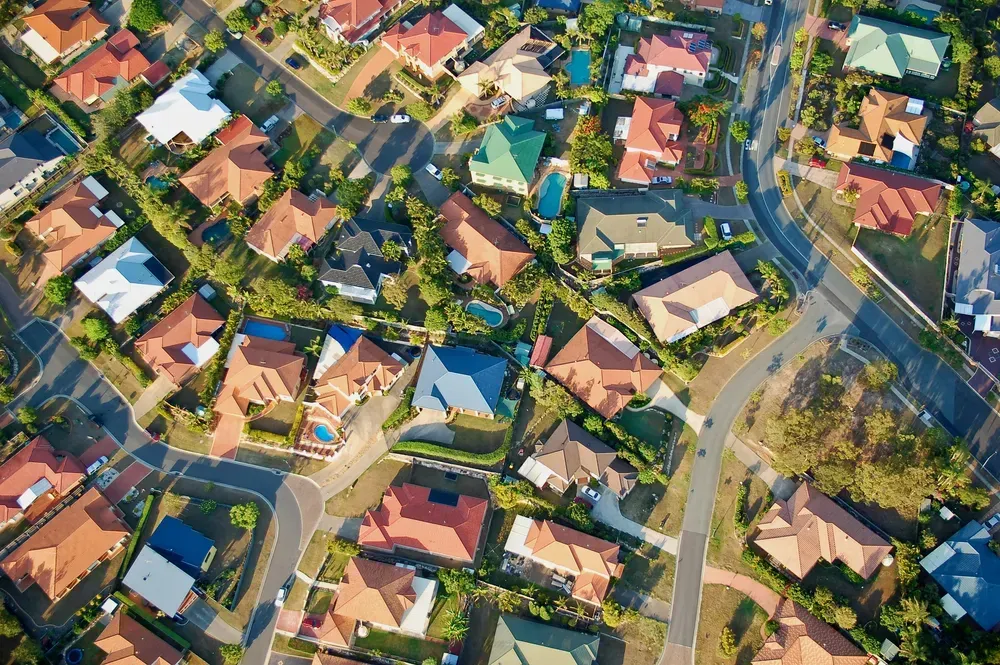 Aerial view of a residential neighborhood with many houses with tiled roofs, surrounded by trees and winding roads. — Diamond Real Estate QLD in North Lakes, QLD