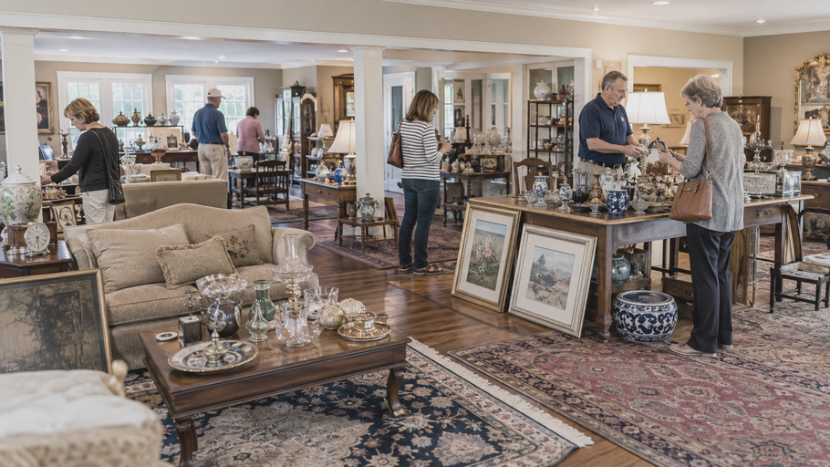 People browsing home decor items in a bright showroom with rugs, tables, and framed artwork.