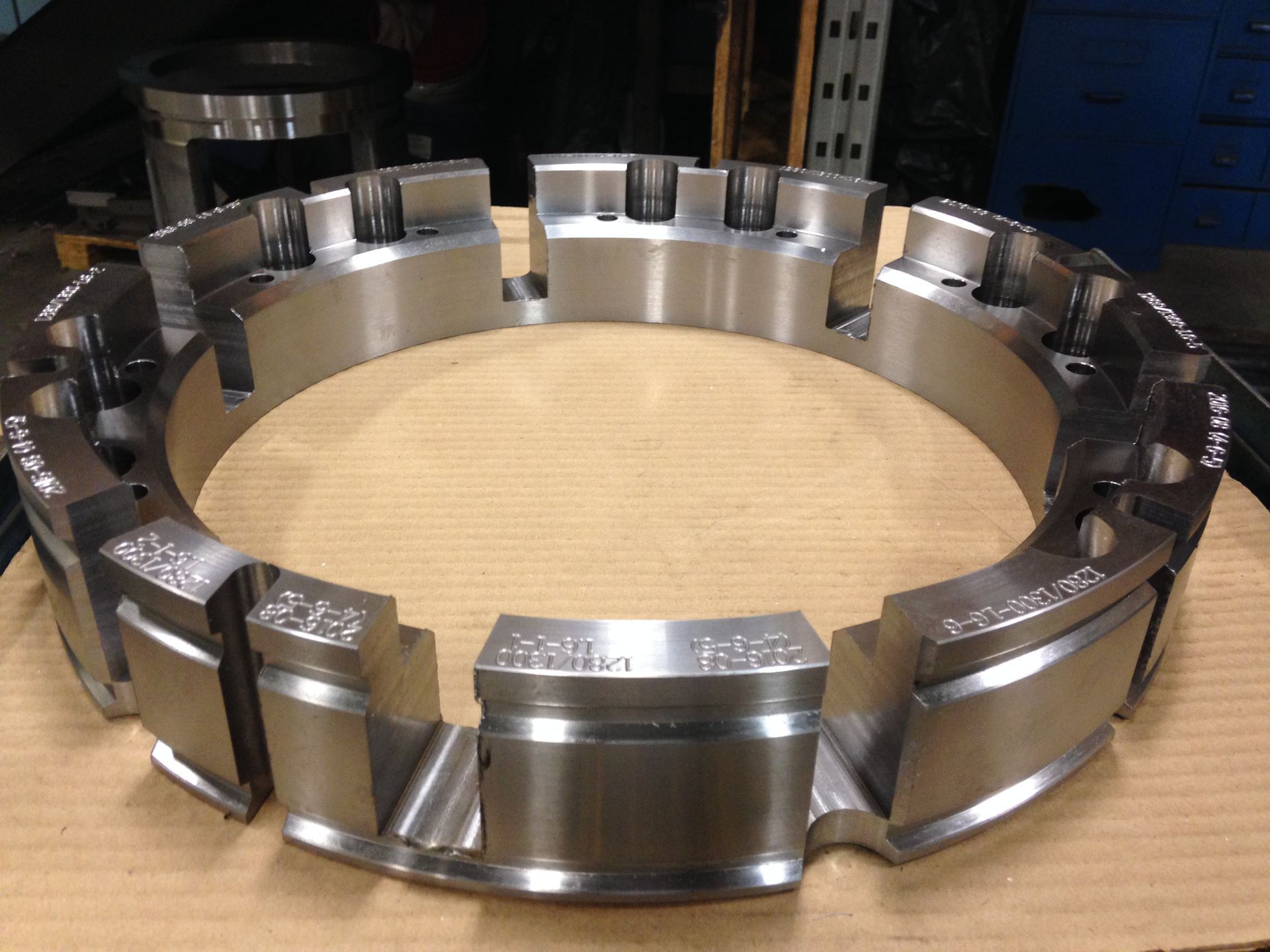 Un grand anneau industriel métallique circulaire avec des blocs rectangulaires surélevés et régulièrement espacés, posé sur un établi en bois.