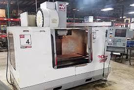 Un centre d'usinage vertical Haas VF-4 blanc est installé dans un atelier, avec un panneau de commande monté sur le côté droit.