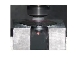 A mechanical punch presses down on a flat metal sheet, causing it to deform downward into a die opening.