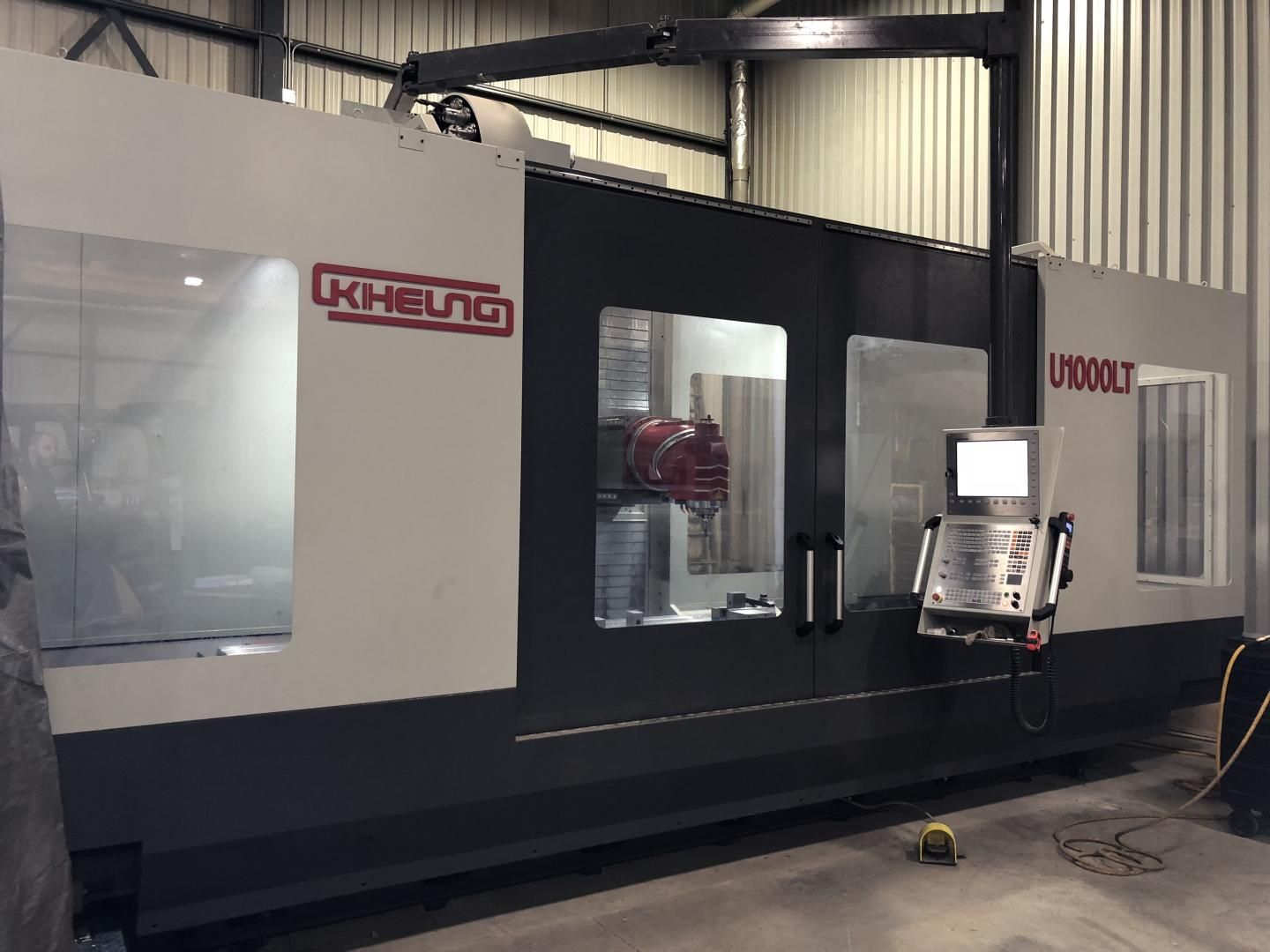Une imposante fraiseuse industrielle CNC grise et noire, équipée d'un panneau de commande, se dresse dans un atelier.