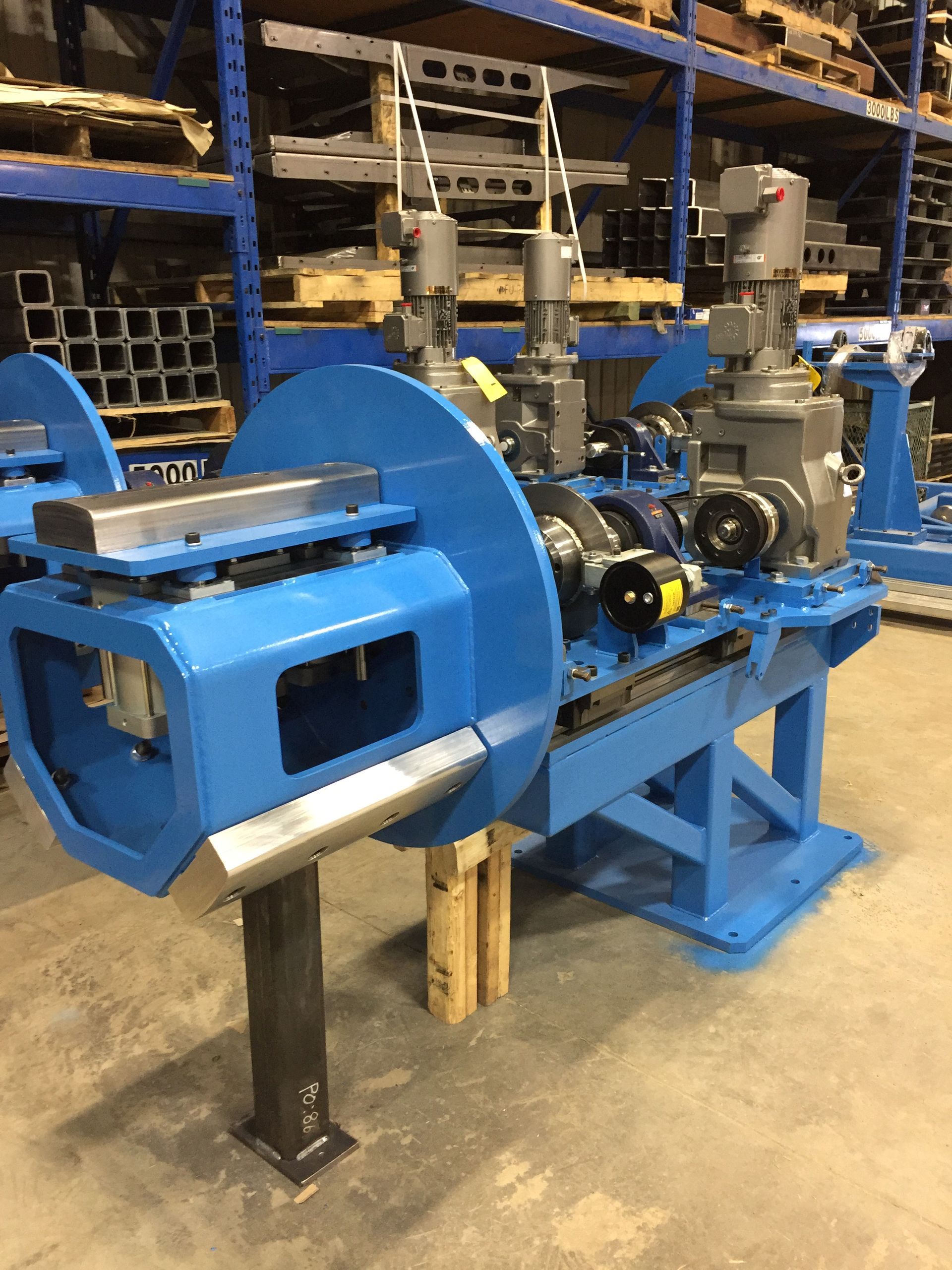 Blue industrial machinery with two motors and a large circular disc, situated on a concrete floor in a warehouse.