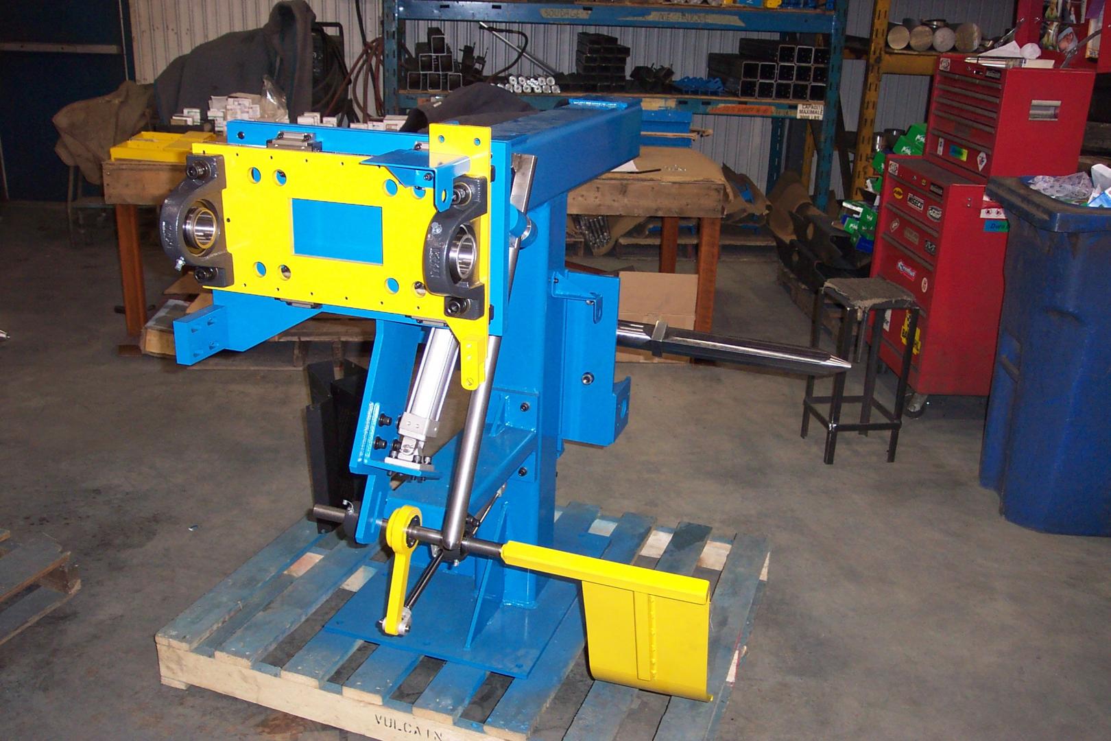 A blue industrial piece of machinery with yellow accents sits on a wooden pallet in a workshop.