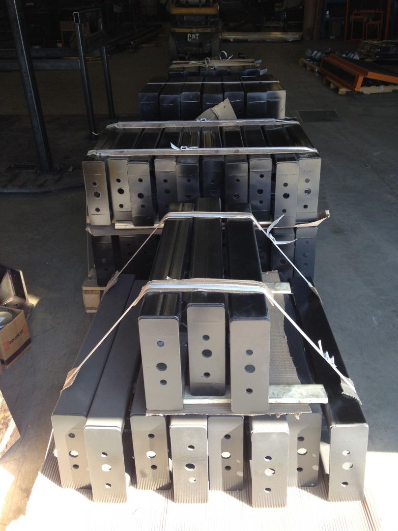 A pallet stacked with rows of dark metal, rectangular structural components, each featuring pre-drilled holes.