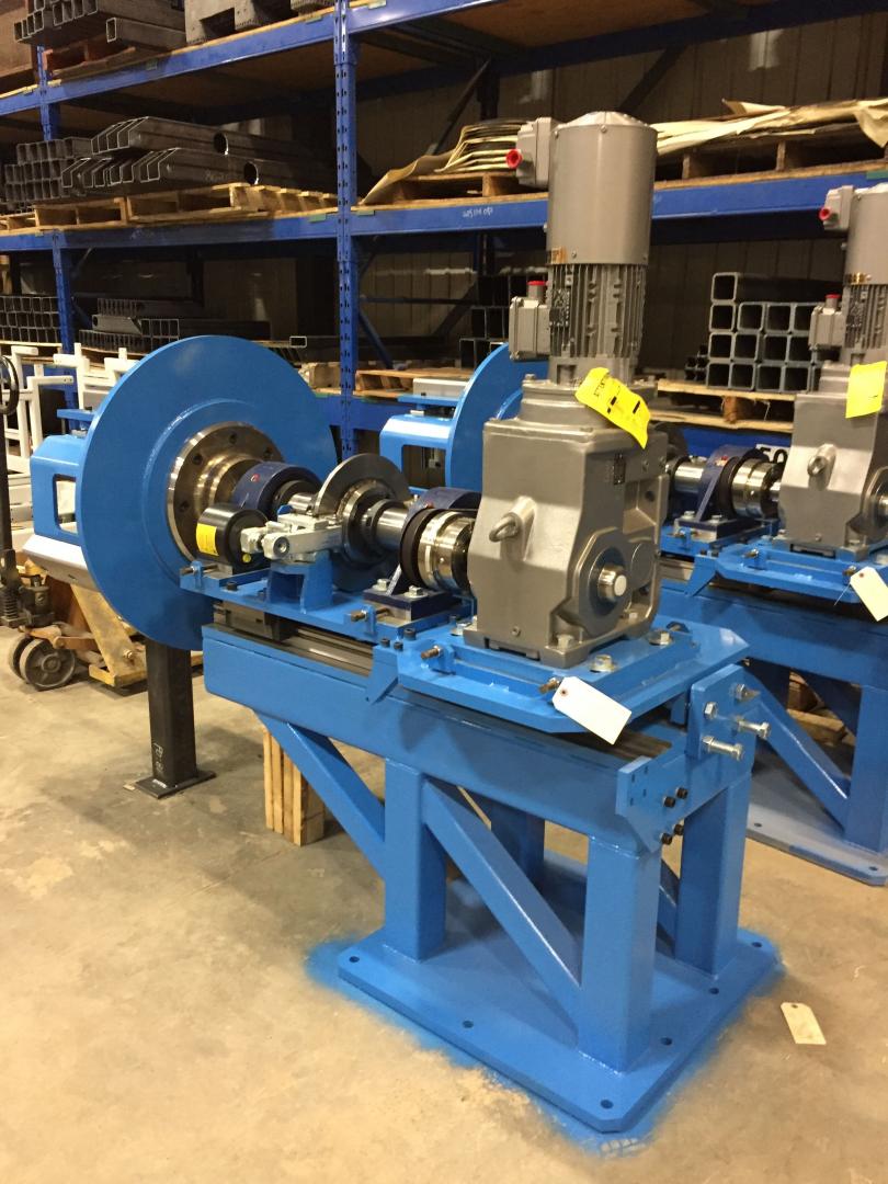 A blue industrial machine with a vertical motor and large wheel, positioned on a factory floor with shelving units.