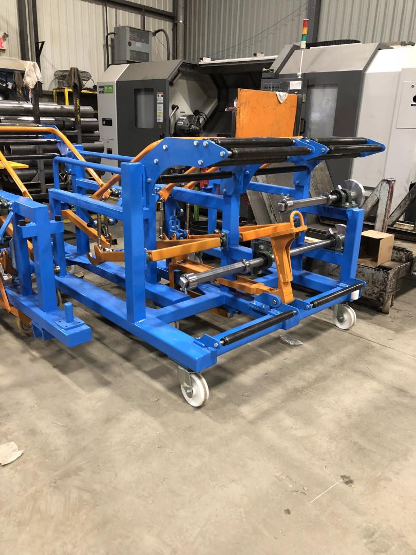A blue, wheeled industrial cart with multiple metal rollers and orange accents, sitting in a manufacturing workshop.