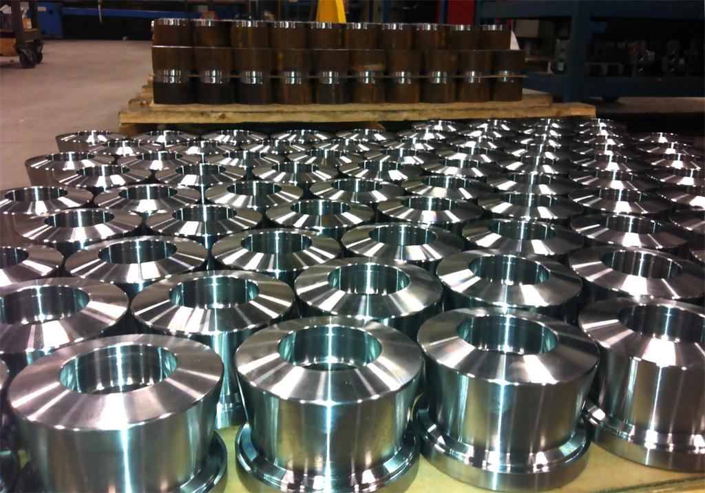 Many shiny, machined metal cylindrical parts arranged in rows on a factory floor.