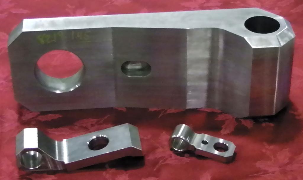 Three machined metal industrial components of varying sizes rest on a red fabric surface.