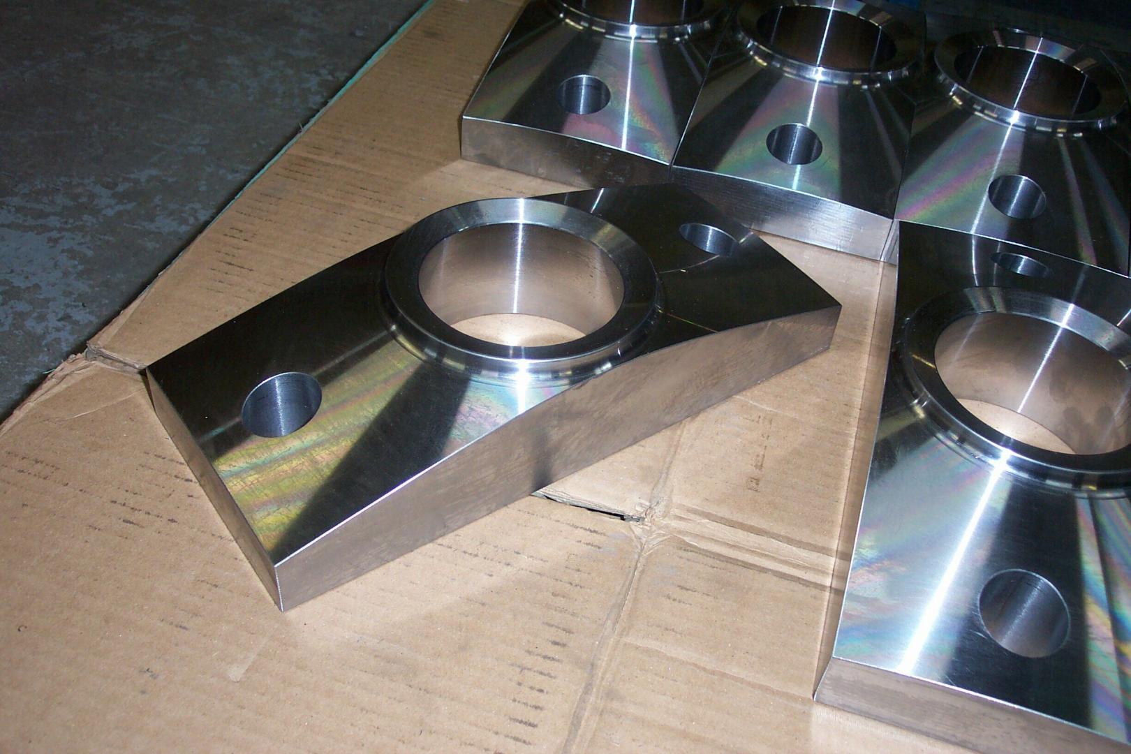 Des pièces industrielles en métal usiné brillant, percées de trous circulaires, reposent sur du carton.