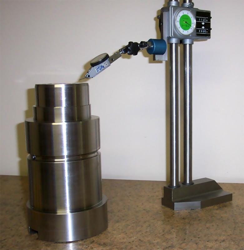 A digital height gauge with an attached dial test indicator measuring a machined metal cylindrical workpiece.