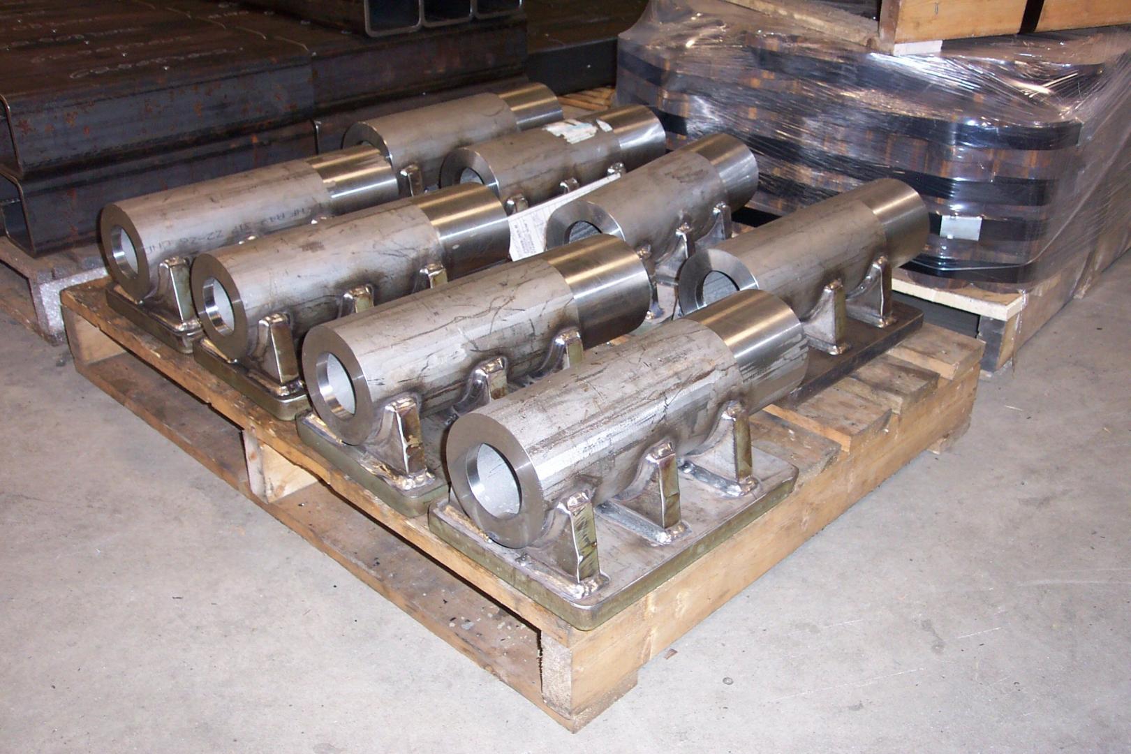 Several cylindrical metal machine parts with mounting brackets arranged on a wooden shipping pallet.